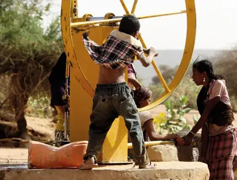 Nigerien children drawing water from a village well with a yellow bucket wheel